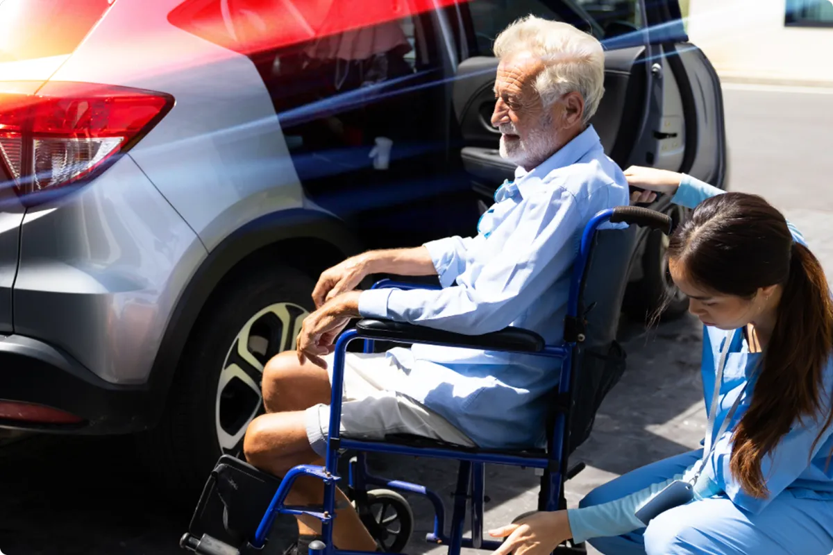 Elderly man in wheelchair receiving assistance from caregiver near vehicle, highlighting compassionate medical transportation services in Livonia.