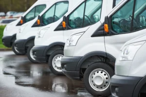 Row of white vans parked on a wet surface.